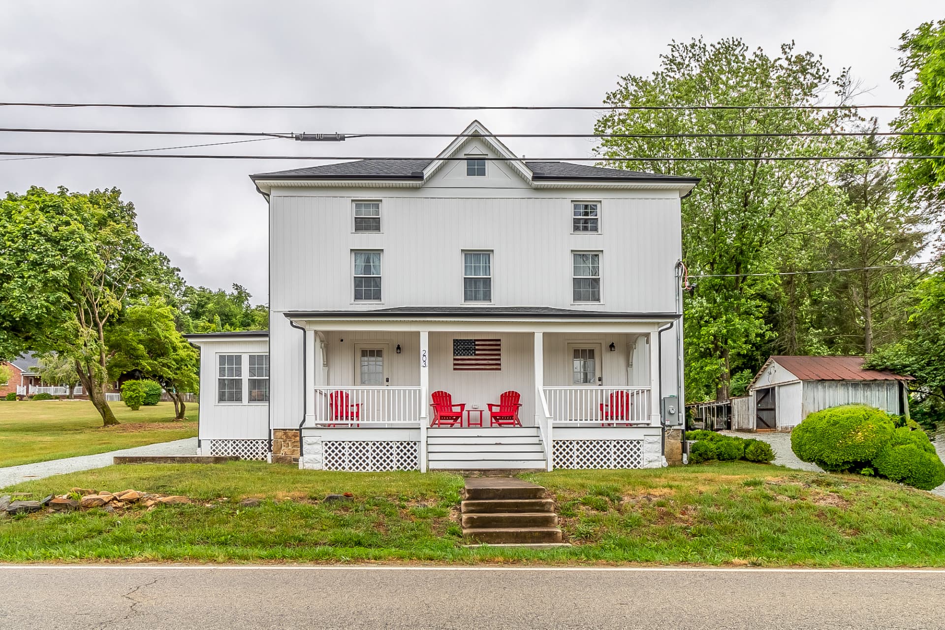 The finished farmhouse from the road with its rebuilt front porch and red chairs