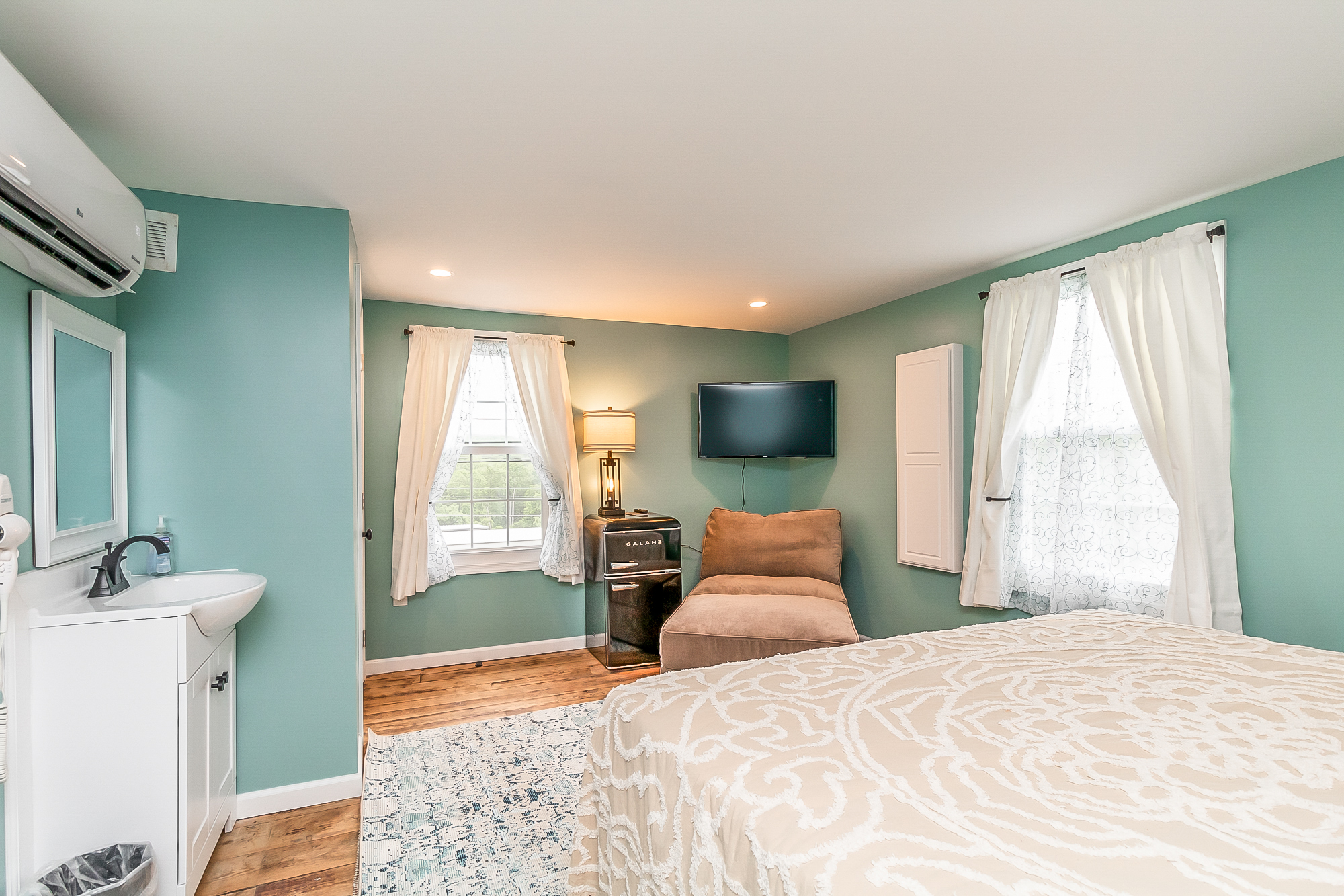 Sea-green bedroom with in-room vanity, TV and lounge chair