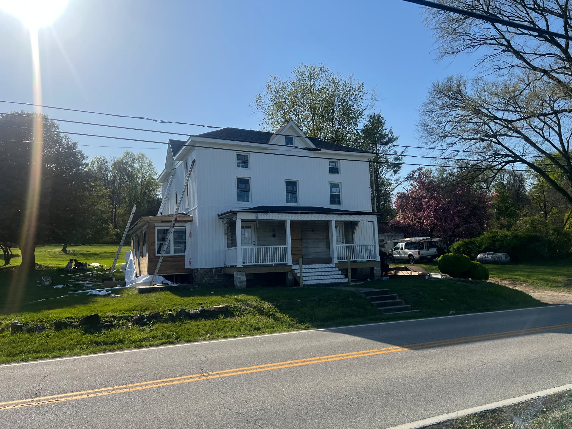 The farmhouse nearly finished in white siding with the porch and sunroom in place