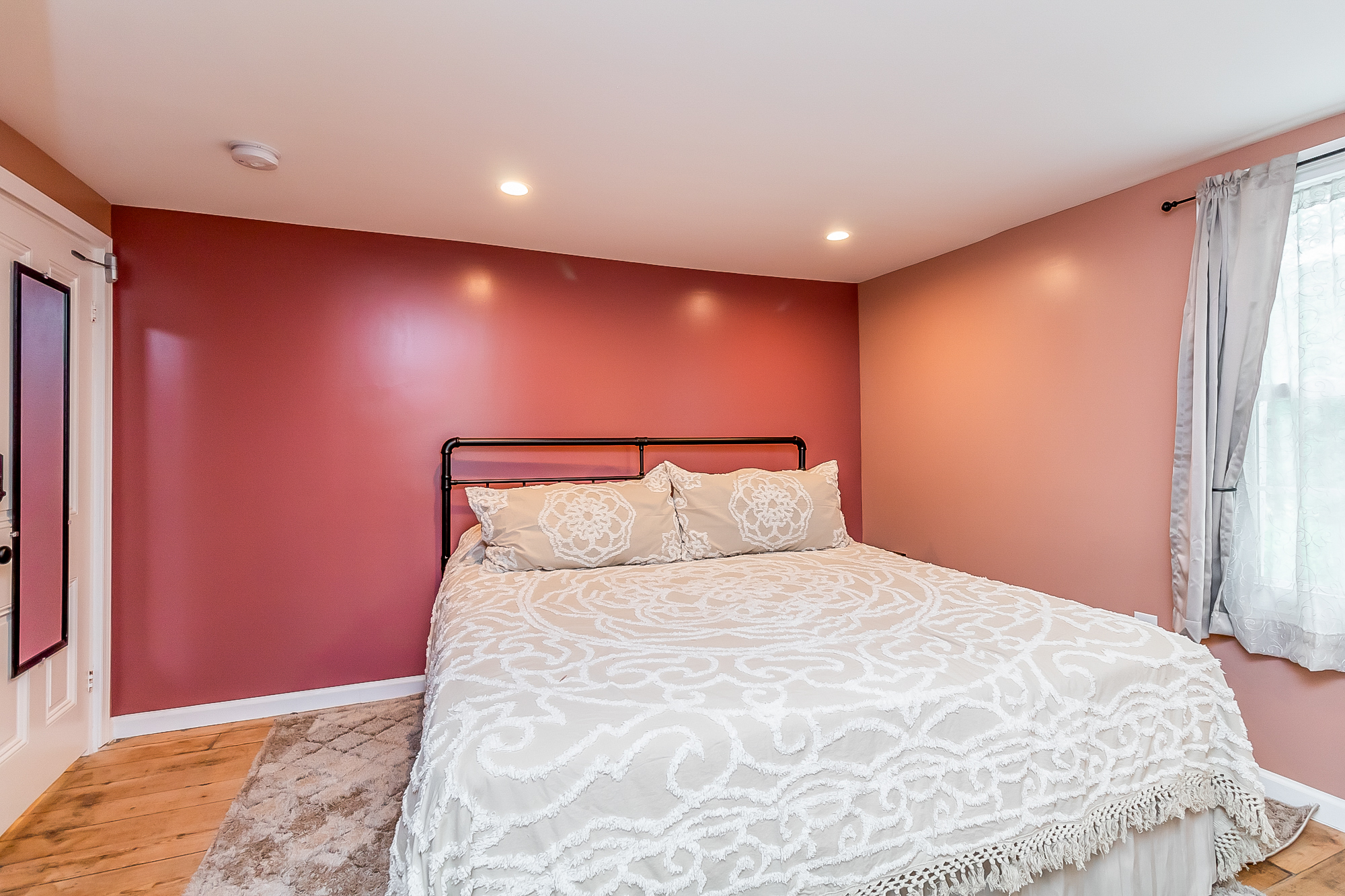 Rose bedroom with iron pipe bed and wide pine floorboards