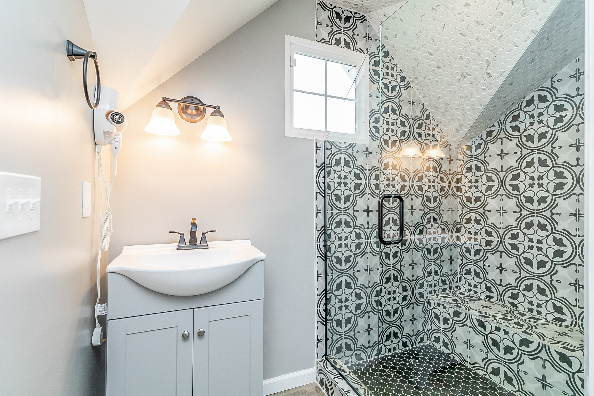 Upstairs bath with vanity and patterned-tile walk-in shower with bench