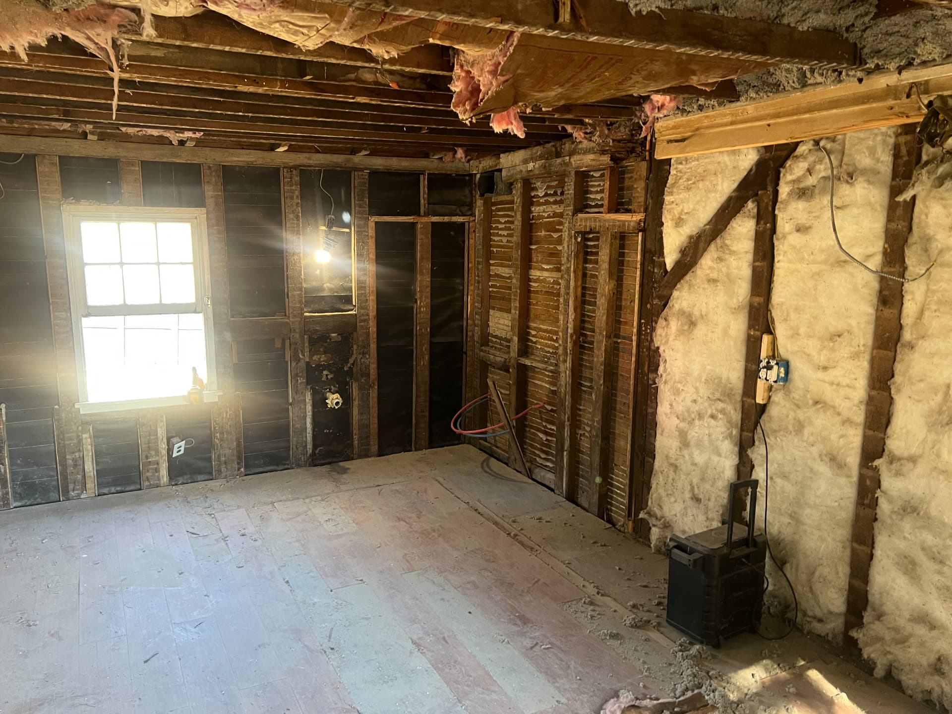 Room stripped to hand-hewn framing and old insulation, subfloor exposed