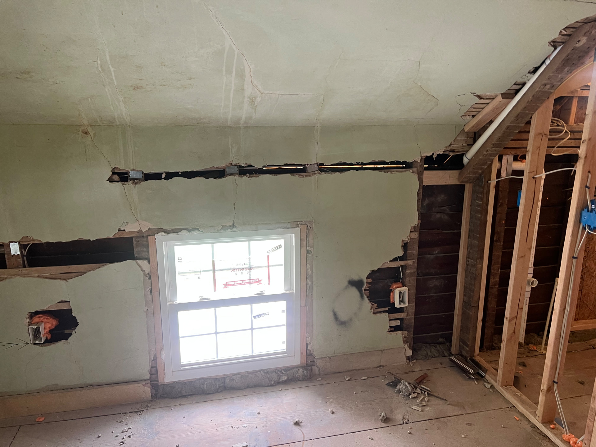 Bedroom wall opened around a new window while a new bath is framed next door