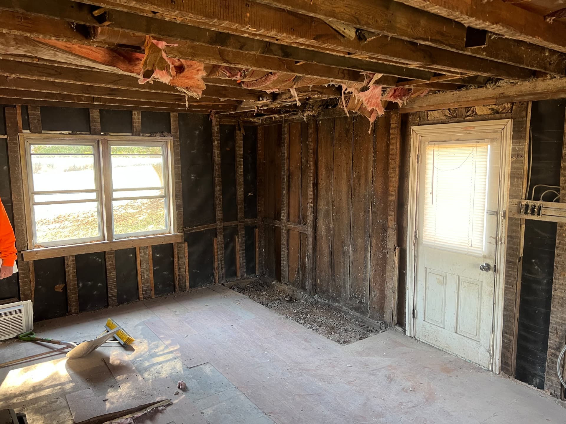 Rear room stripped to bare framing with windows and door still in place